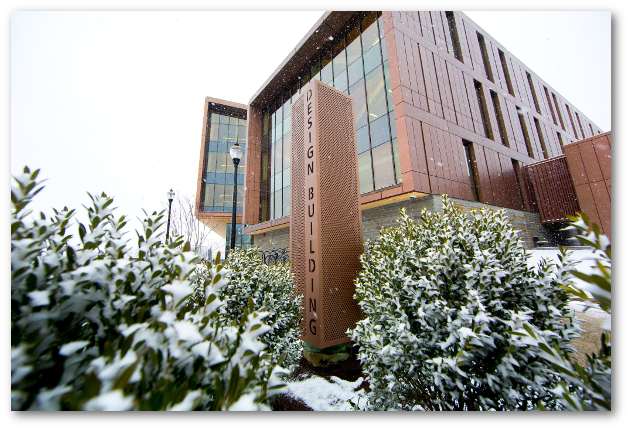 Looing up at the Olver Design Building from ground level. Evergreen trees in the foreground have a dusting of snow.