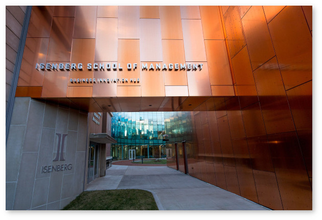 Entrance to Isenberg School of Management. The overhead sign has a background field of copper tiles. The view is inside towards an interior lobby.