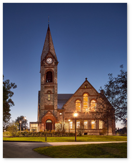 A clear, dark blue sky surrounds Old Chapel at late dusk. Illuminated windows and streetlights add light and sparkle to the image.