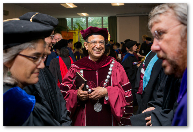 Chancellor Subbaswamy talks to two faculty members during convocation. All are wearing academic robes.