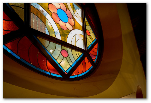 Round stained glass window with square interior frame featuring rounded geometric shapes