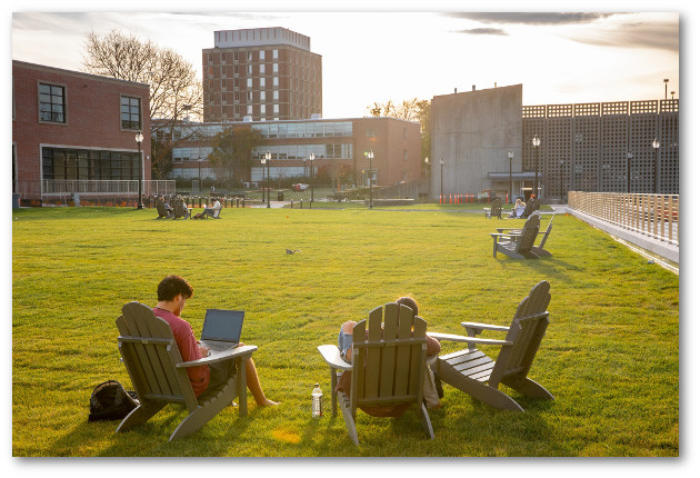 Students relax and study in Adirondack chairs in small groups on lawn next to Student Union building
