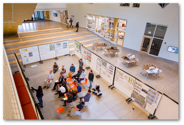 Class meeting in lobby of Design building. Meeting space is defined by panels displaying projects.