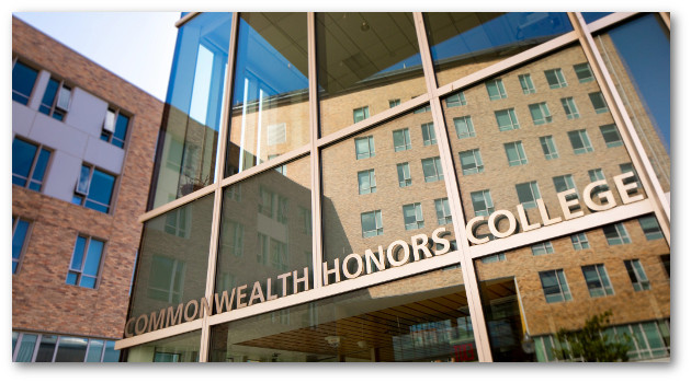 Glass front of Commonwealth Honors College building with sign above door and neighboring building reflecting in the glass