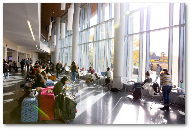 Students chat and eat in the Integrative Learning Center's cafe and comon space. Sun streams in through a tall wall of windows.