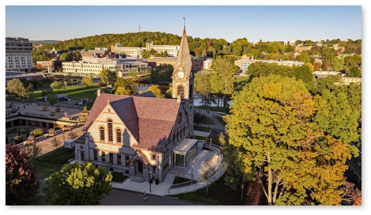 Aerial view of Old Chapel looking northeast towards the Campus Center and academic buildings. Long evening shadows fall on the sides of Old Chapel and cloak much of the ground in shadow while sunlight illuminates the treetops.