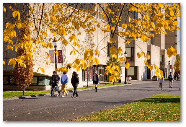 Small groups of students walk past Herter Hall. Yellow fall leaves frame the image.
